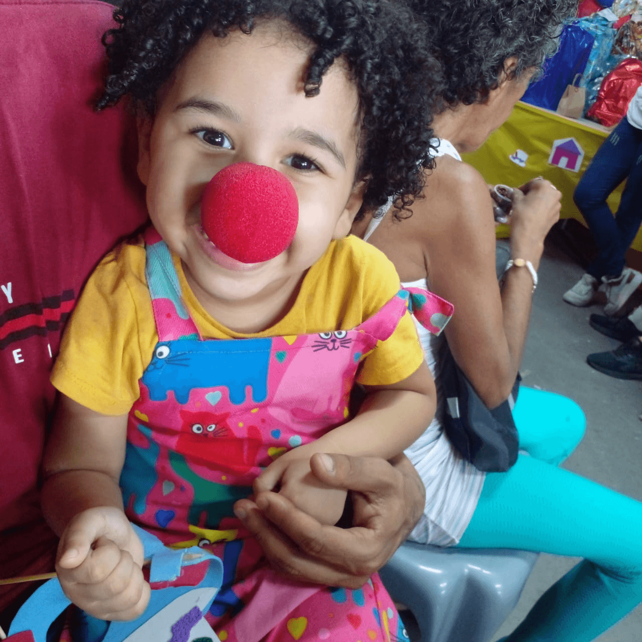 Criança sorrindo com nariz vermelho de palhaço em uma ação da ACAI